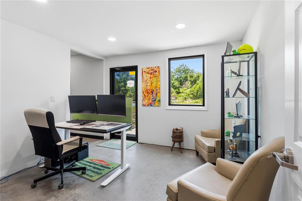 A home office features a standing desk, two armchairs, a glass display cabinet, and concrete floors — 15617 OLD US HIGHWAY 441, TAVARES, FL