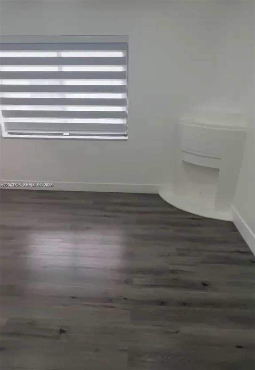 A room with gray wood-look flooring, white walls, a window with blinds, and a corner fireplace — 1895 SW 22nd # 7, Miami FL 33145, MIAMI, FL