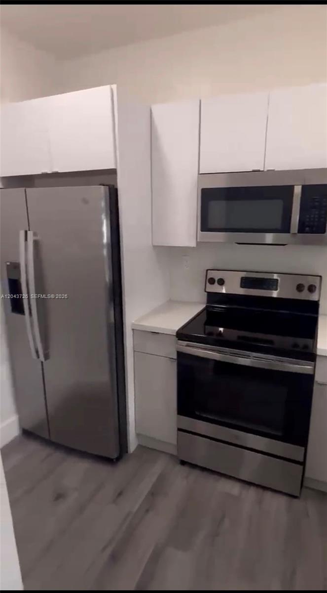 A kitchen features stainless steel appliances, white cabinets, and light-colored wood-look flooring — 1895 SW 22nd # 7, Miami FL 33145, MIAMI, FL