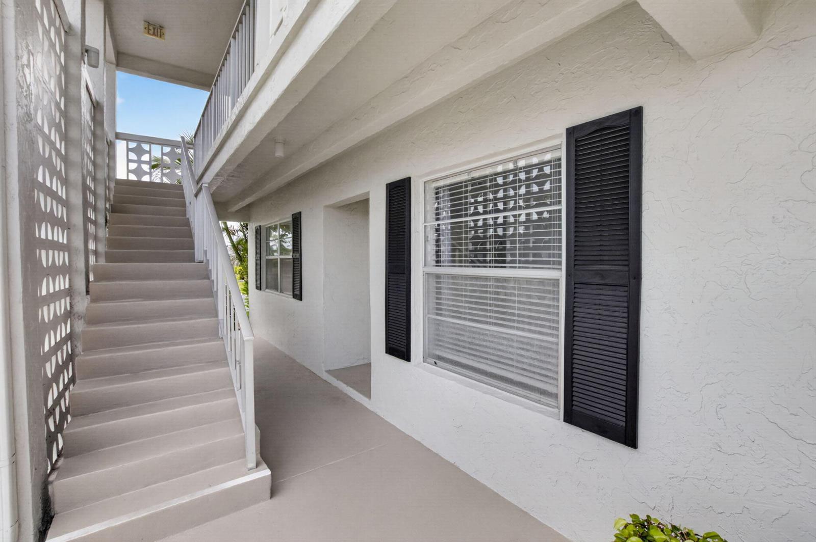 An exterior view of a building with a concrete staircase, white walls, and black shutters — 2401 Del Aire Boulevard # 101, Delray Beach FL 33445, DELRAY BEACH, FL