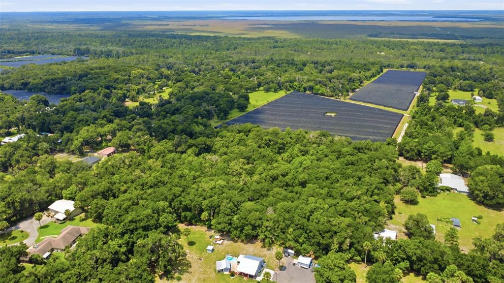 An aerial view shows a rural property with large shade-covered agricultural fields and surrounding woods — GRAND AVENUE, DELAND, FL