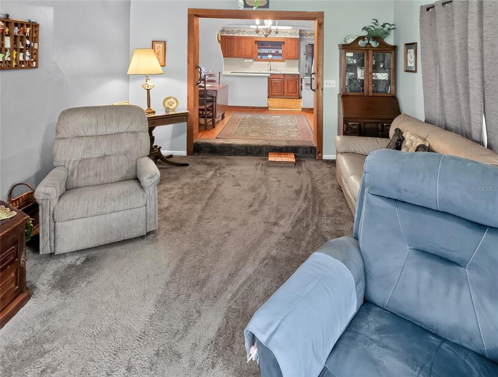 A living room with gray carpet, two recliners, and a doorway leading to a kitchen — 32805 LAKE EUSTIS DRIVE, TAVARES, FL