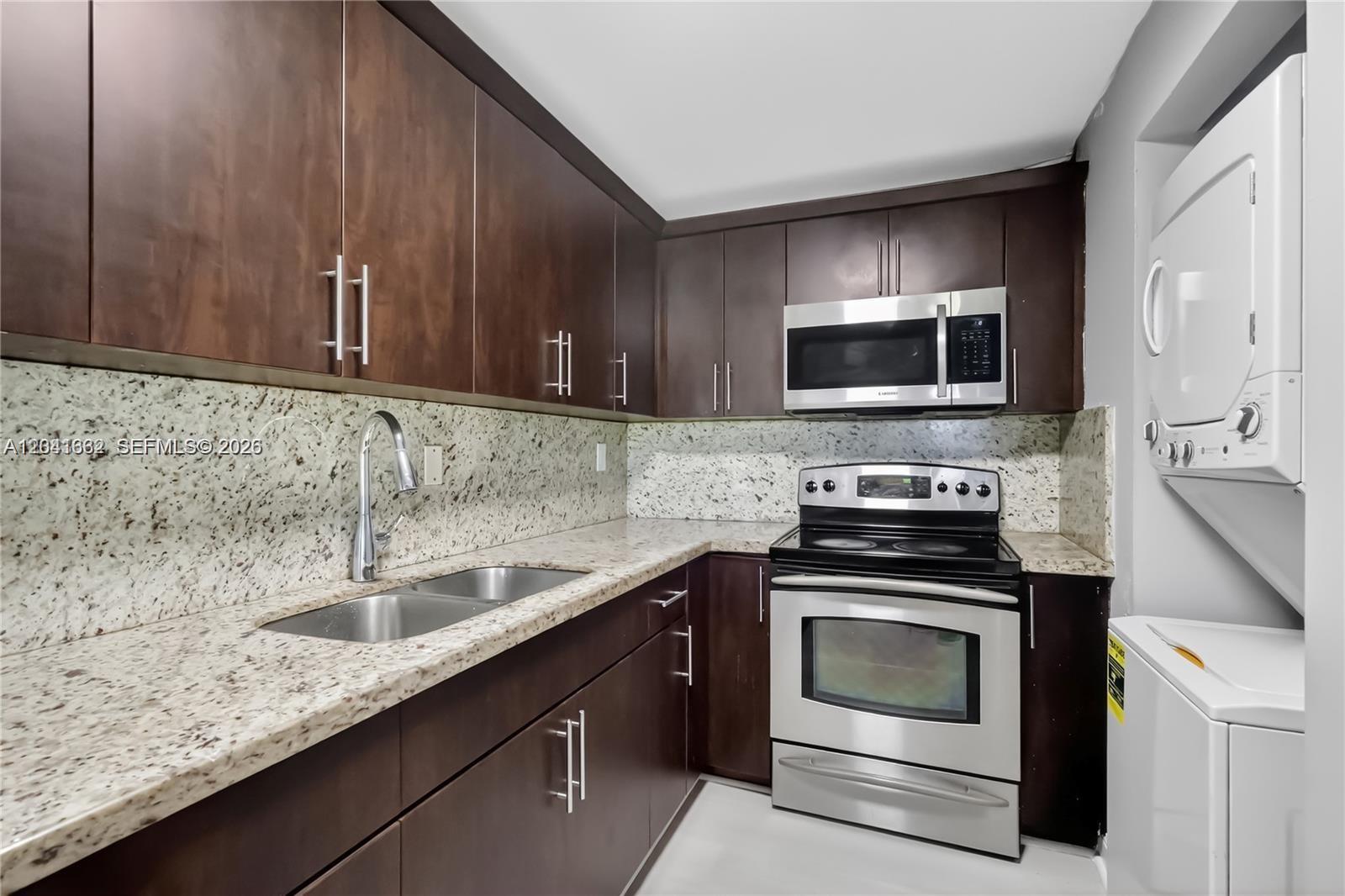 A kitchen features dark wood cabinets, granite countertops, stainless steel appliances, and a stacked washer-dryer — HIALEAH GARDENS, FL