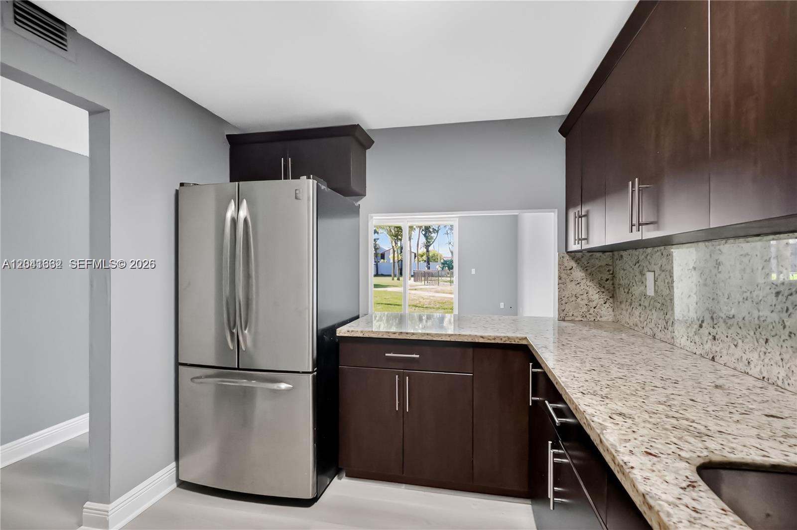 A kitchen features dark wood cabinets, granite countertops, stainless steel appliances, and a pass-through window — HIALEAH GARDENS, FL