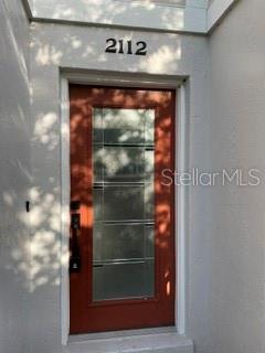 A red front door with a vertical glass panel sits below the house number 2112 — 2112 NE 38TH AVENUE, OCALA, FL