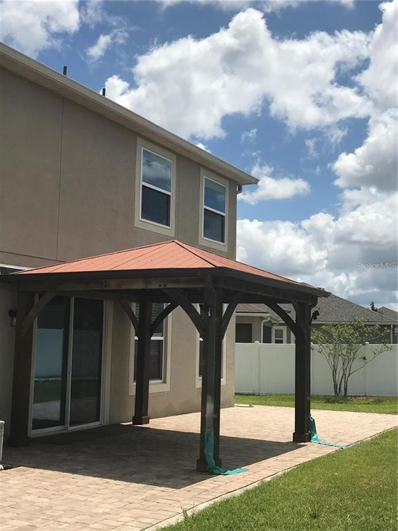 A wooden gazebo with a red metal roof stands on a paved patio behind a house — 2504 AMATI DRIVE, KISSIMMEE, FL