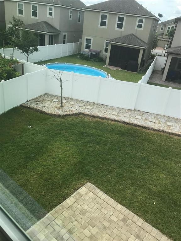 A backyard features a green lawn, a stone patio, a white fence, and a pool — 2504 AMATI DRIVE, KISSIMMEE, FL