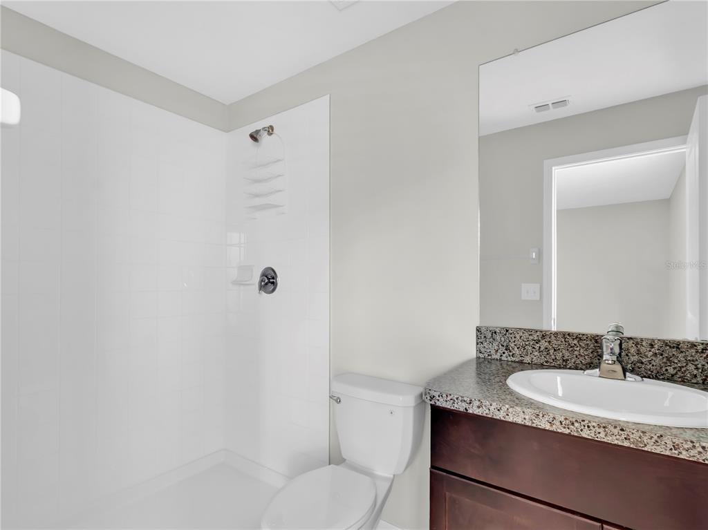 A bathroom features a white tiled shower, a toilet, and a vanity with a granite countertop — 16568 DELIA STREET, WIMAUMA, FL