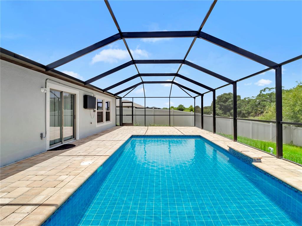 A rectangular swimming pool sits inside a screened-in lanai with light-colored paver decking — 16568 DELIA STREET, WIMAUMA, FL