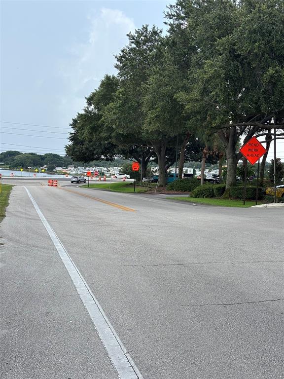A paved road leads toward a waterfront area with trees and road work signage — 12 HEARTLAND DRIVE, LAKE PLACID, FL