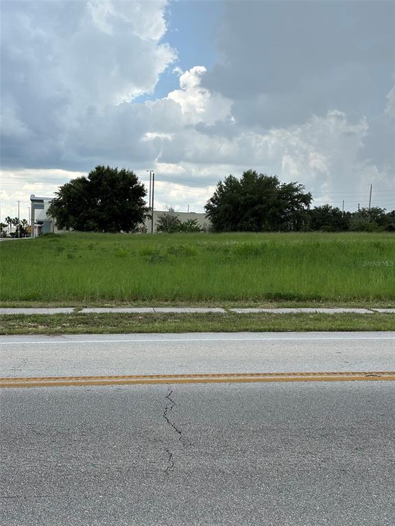 A vacant, grassy lot sits alongside a paved road under a cloudy sky — 12 HEARTLAND DRIVE, LAKE PLACID, FL