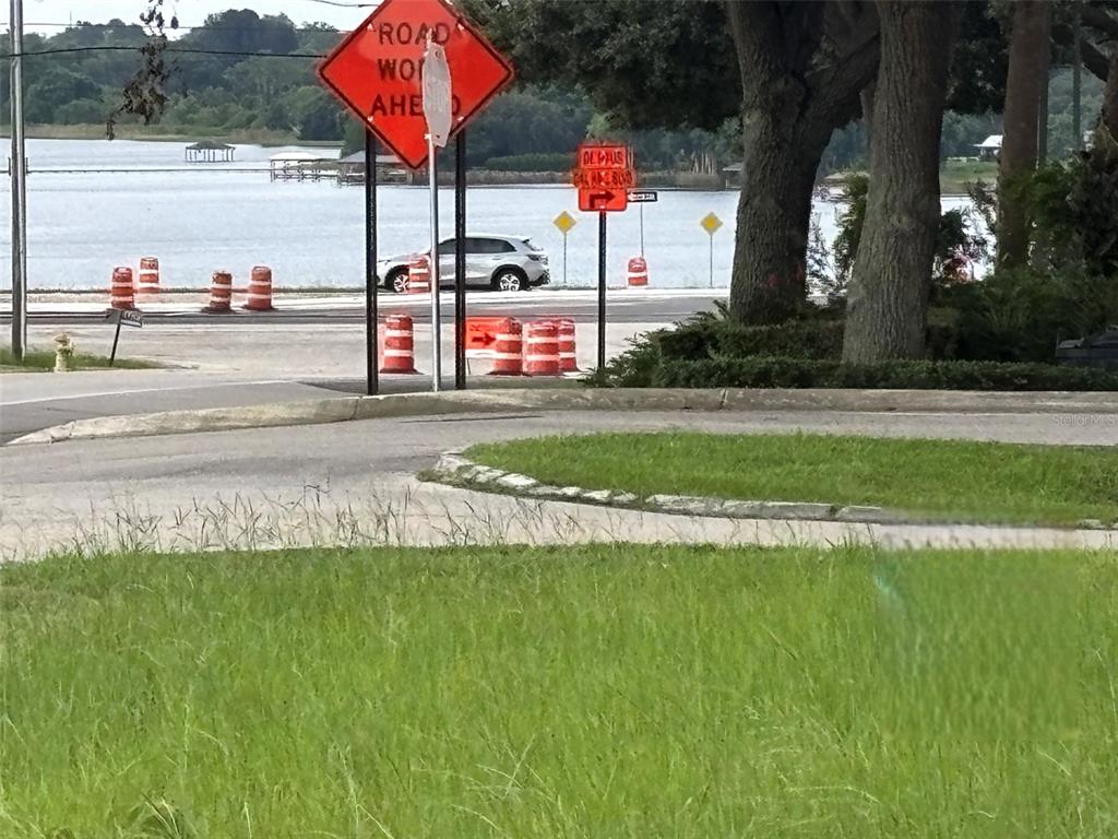 A road construction zone with orange signs and traffic barrels sits beside a lake — 12 HEARTLAND DRIVE, LAKE PLACID, FL