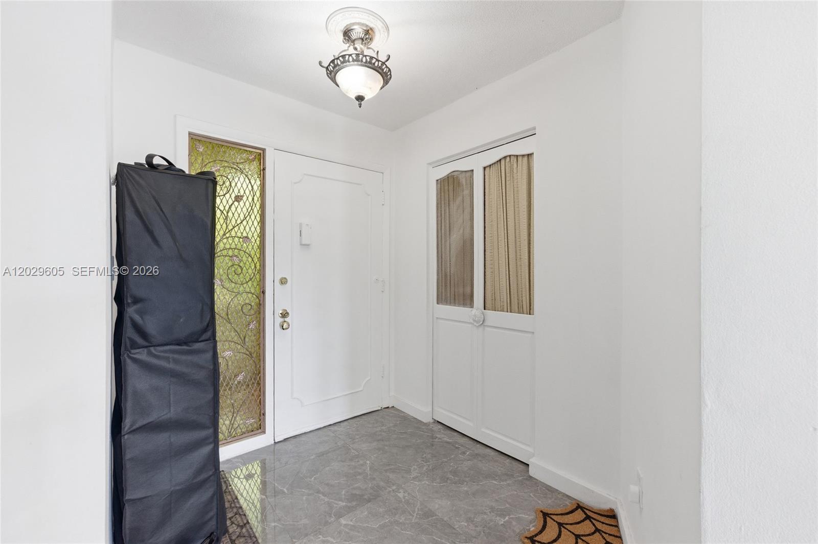 An entryway features a white door with a decorative glass panel, tile flooring, and closet — 1501 NE 191st St # C217, Miami FL 33179, MIAMI, FL