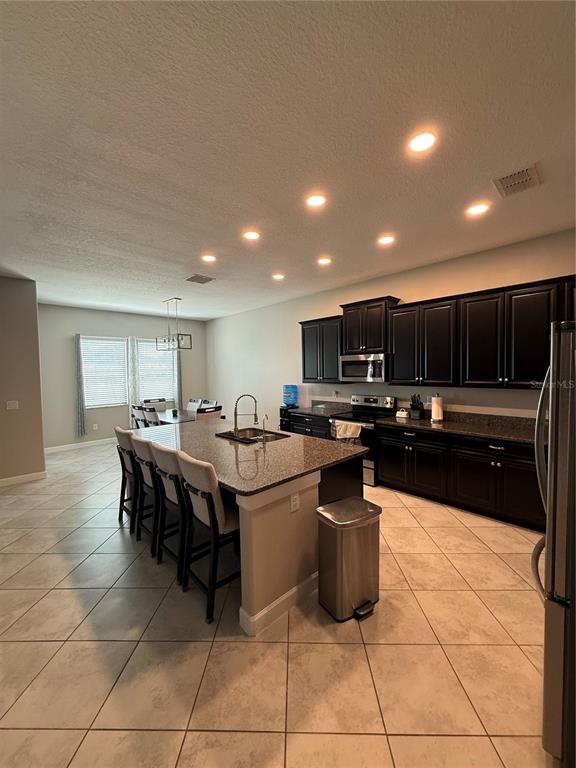 A kitchen with dark cabinets, granite countertops, a center island with seating, and tile flooring — 11612 SUNBURST MARBLE ROAD, RIVERVIEW, FL