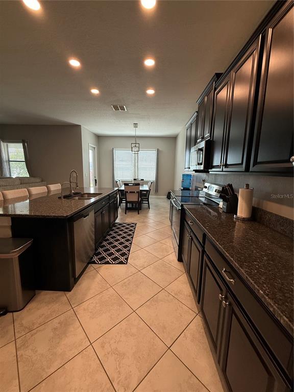 A kitchen features dark cabinetry, granite countertops, a large island, and tile flooring — 11612 SUNBURST MARBLE ROAD, RIVERVIEW, FL