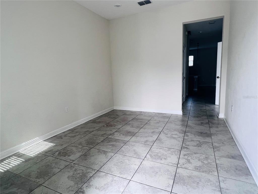 An empty room with light gray tile flooring and white walls leads into a hallway — 4894 TRIBUTE TRAIL, KISSIMMEE, FL