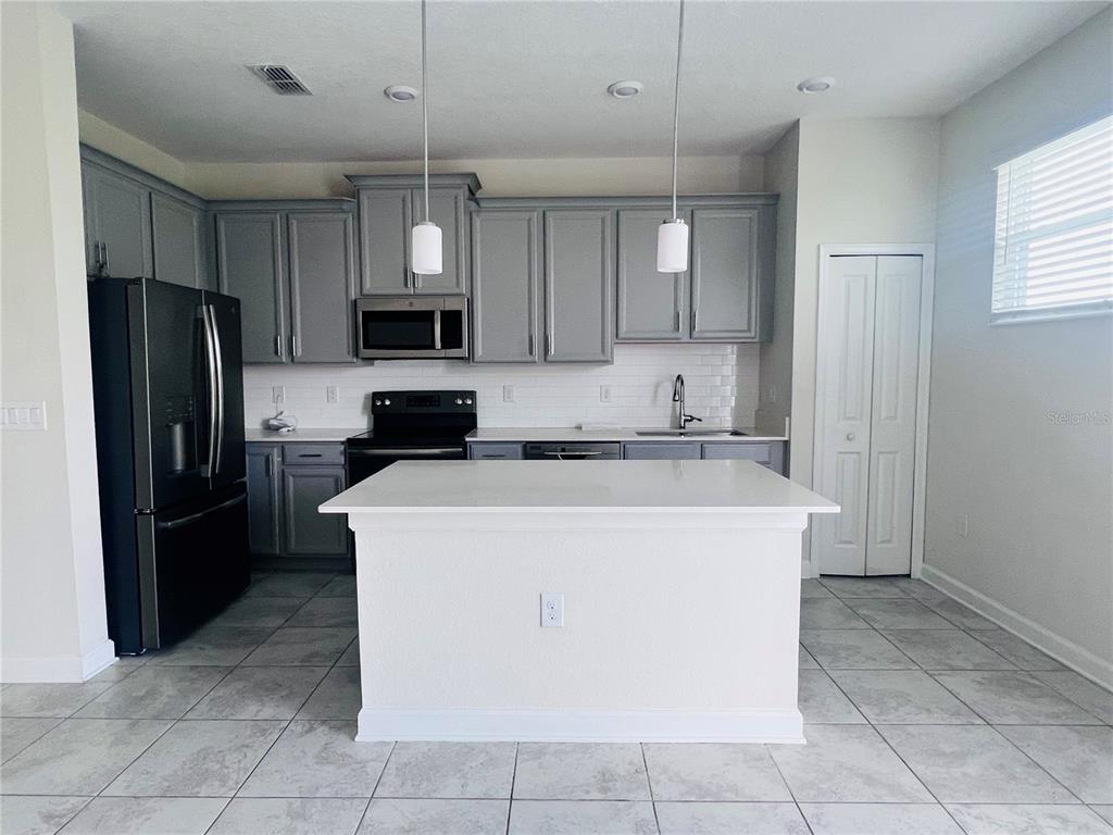 A kitchen features grey cabinets, a white island, stainless steel appliances, and tile flooring — 4894 TRIBUTE TRAIL, KISSIMMEE, FL