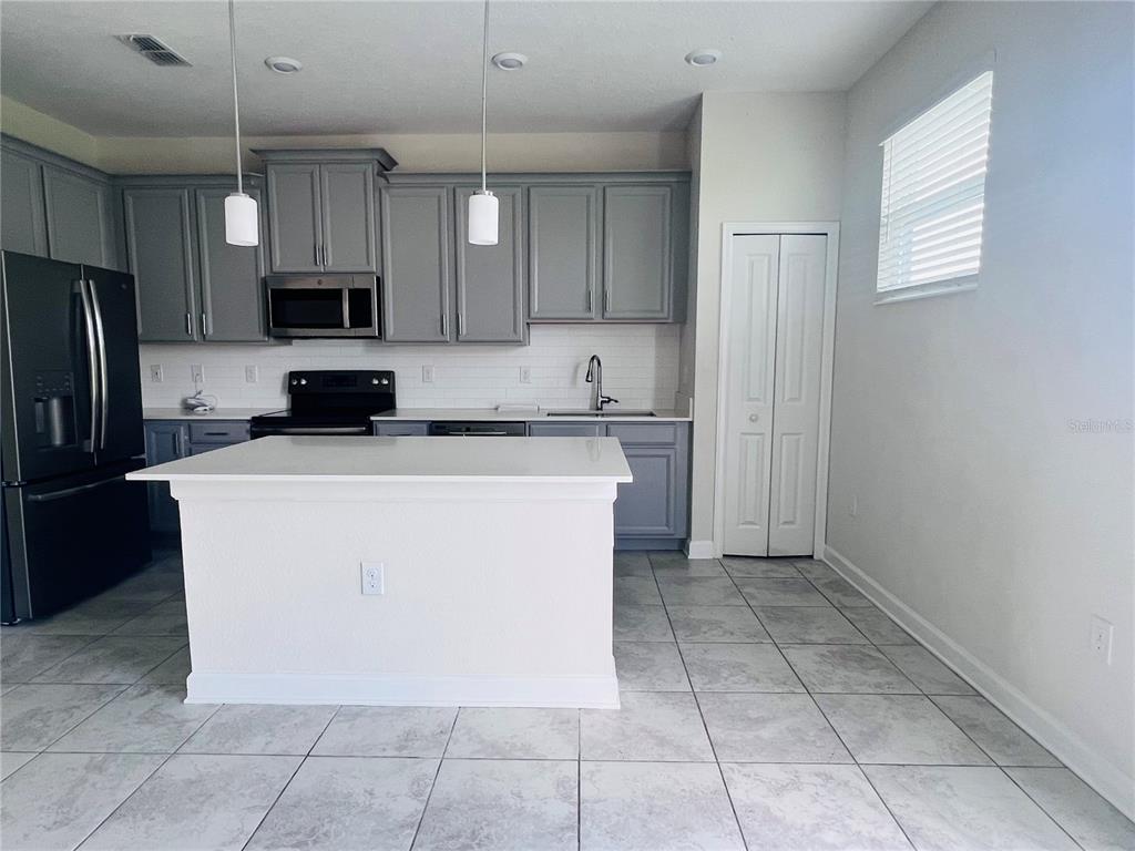 A kitchen features gray cabinets, a white island, stainless steel appliances, and tile flooring — 4894 TRIBUTE TRAIL, KISSIMMEE, FL