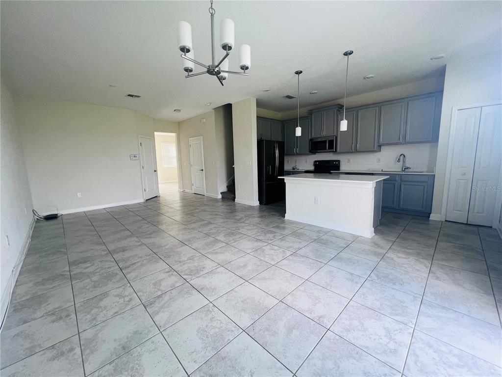 An open-concept kitchen and living area features gray cabinets, a white island, and tiled floors — 4894 TRIBUTE TRAIL, KISSIMMEE, FL