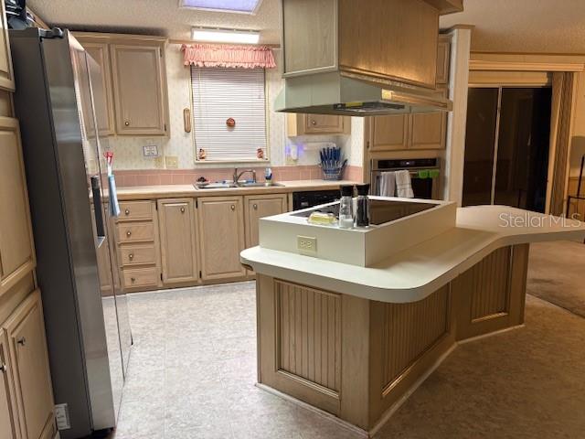A kitchen features light wood cabinets, a central island with a cooktop, and stainless appliances — 4412 TEKA LANE, ST CLOUD, FL