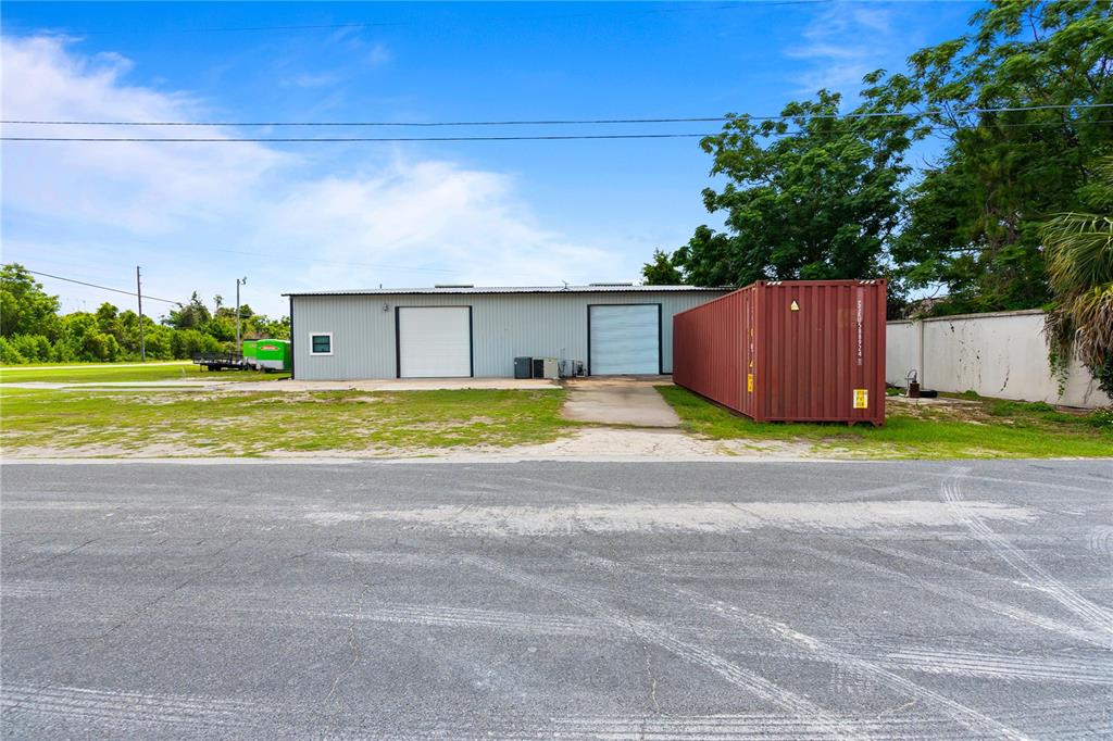 A metal warehouse building features two roll-up doors and an adjacent red shipping container — 15601 OLD US HIGHWAY 441, TAVARES, FL