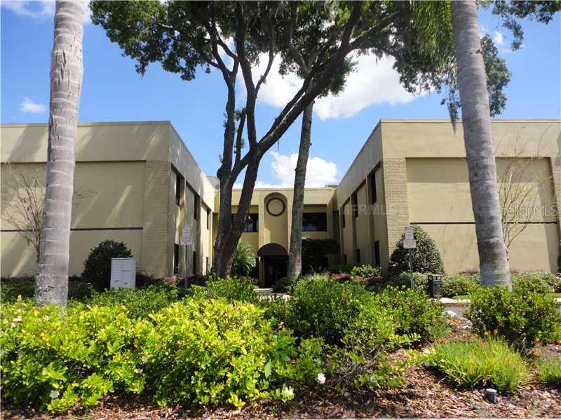 A two-story tan commercial building is framed by palm trees and lush landscaping — 36739 COUNTY ROAD 52 UNIT 203, DADE CITY, FL