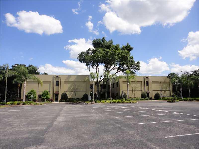 A two-story commercial building with a large parking lot and palm trees under a blue sky — 36739 COUNTY ROAD 52 UNIT 203, DADE CITY, FL