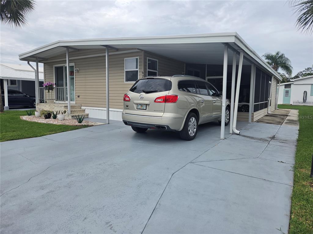 A tan mobile home features a concrete driveway, a carport, and a screened-in porch area — 628 LAKESIDE RANCH LANE, WINTER HAVEN, FL