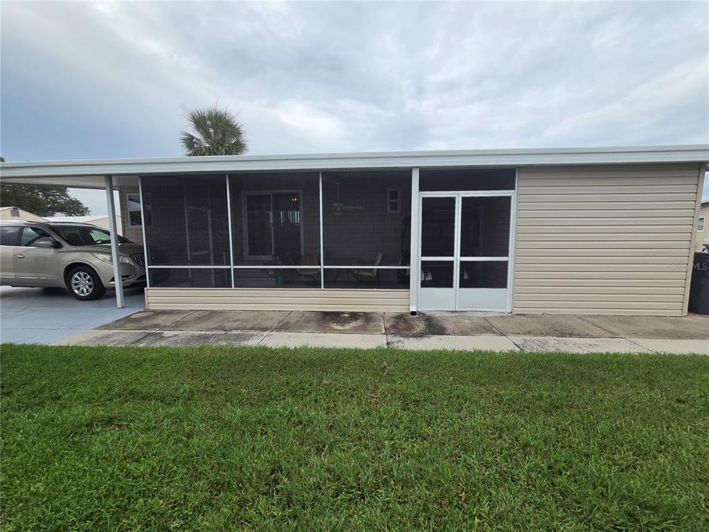 A beige manufactured home features a screened-in porch and an attached carport with a parked car — 628 LAKESIDE RANCH LANE, WINTER HAVEN, FL