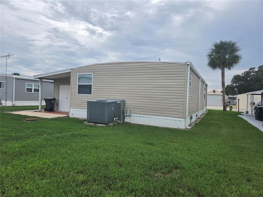 The exterior of a beige mobile home features a side entrance, an air conditioning unit, and lawn — 628 LAKESIDE RANCH LANE, WINTER HAVEN, FL