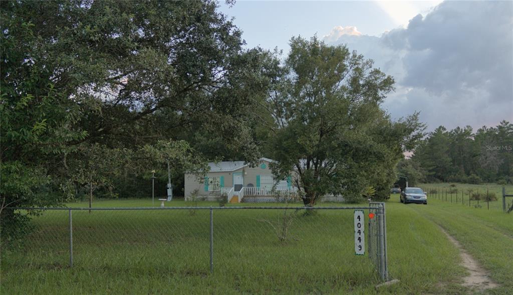 A single-story house sits behind a chain-link fence on a grassy lot with mature trees — 40449 HOLLY BRANCH ROAD, EUSTIS, FL