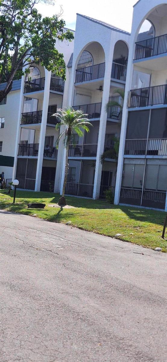 A multi-story apartment building with arched balconies and a palm tree on the front lawn — 3300 Spanish Moss Terrace # 402, Lauderhill FL 33319, LAUDERHILL, FL