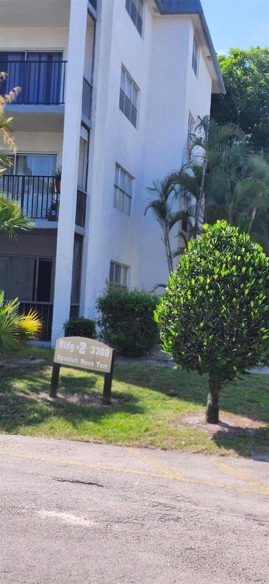 A multi-story white apartment building stands behind a sign labeled Building 2 3300 — 3300 Spanish Moss Terrace # 402, Lauderhill FL 33319, LAUDERHILL, FL