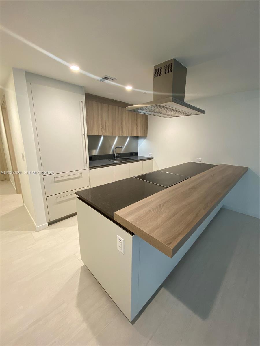 A modern kitchen features white cabinetry, a dark countertop island, and a wood-toned breakfast bar — 1000 Brickell Plaza # 2007, Miami FL 33131, MIAMI, FL