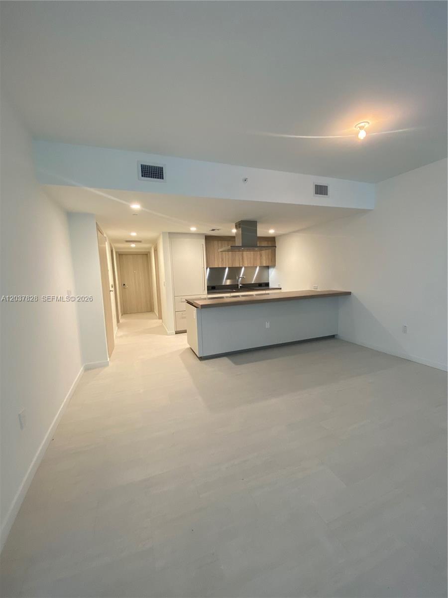 This open-concept kitchen features a breakfast bar, stainless steel hood, and light-colored flooring — 1000 Brickell Plaza # 2007, Miami FL 33131, MIAMI, FL