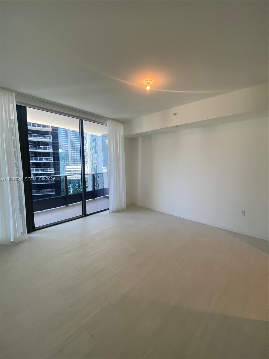 An empty room with light wood floors, white walls, and a sliding glass door balcony — 1000 Brickell Plaza # 2007, Miami FL 33131, MIAMI, FL