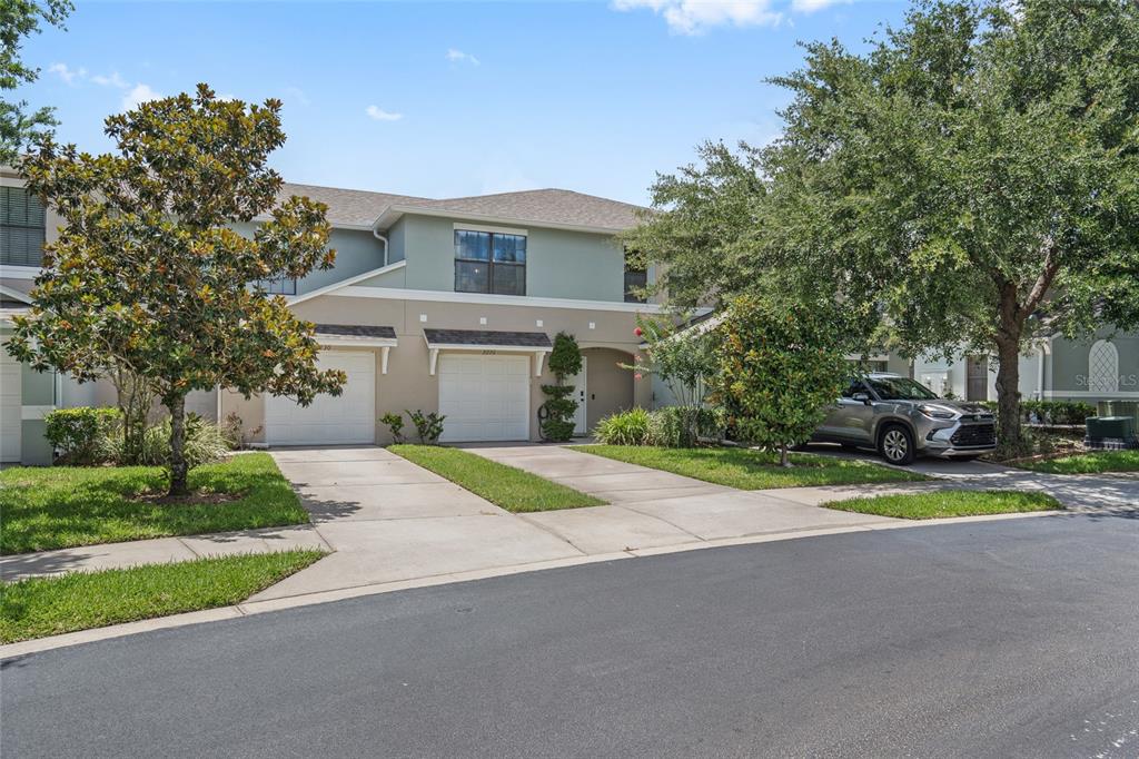 A two-story townhouse with two garages, concrete driveways, and surrounding trees under a blue sky — 2220 WINDSOR LAKE CIRCLE, SANFORD, FL
