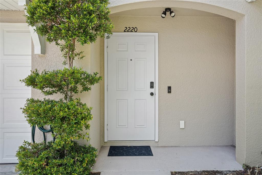 A white front door with a keypad lock is set into a beige stucco exterior — 2220 WINDSOR LAKE CIRCLE, SANFORD, FL