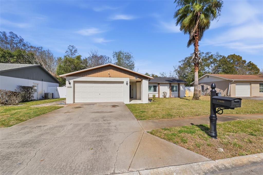 A single-story house with a beige exterior, a two-car garage, and a palm tree — 11608 FOX RUN, PORT RICHEY, FL