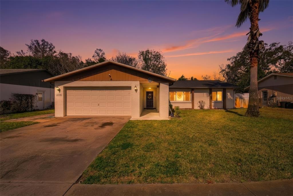 A single-story house with a white brick facade, brown trim, and a concrete driveway at sunset — 11608 FOX RUN, PORT RICHEY, FL
