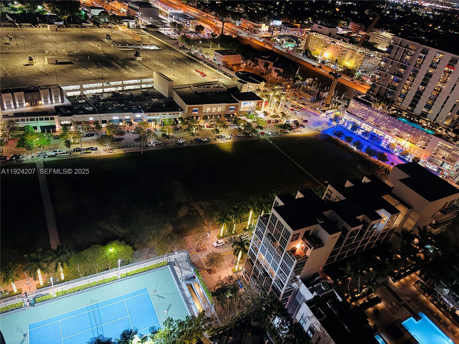 An aerial night view shows a tennis court, apartment buildings, and a nearby shopping center — 121 NE 34th St # 3014, Miami FL 33137, MIAMI, FL