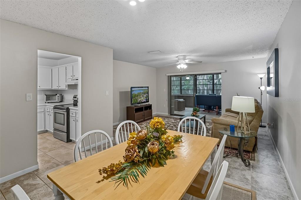 A living room features a tan sofa, patterned area rug, ceiling fan, and sliding glass doors — 2746 SW 14 DRIVE UNIT 2746, GAINESVILLE, FL
