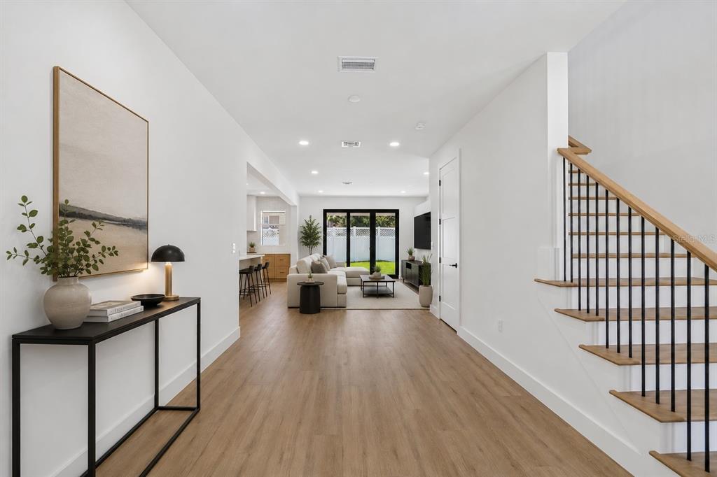 A bright hallway leads to an open-concept living area with wood floors and a staircase — 6403 S RICHARD AVENUE, TAMPA, FL