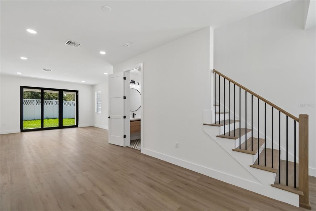 A bright room with light wood flooring, a staircase with black railings, and a bathroom doorway — 6403 S RICHARD AVENUE, TAMPA, FL