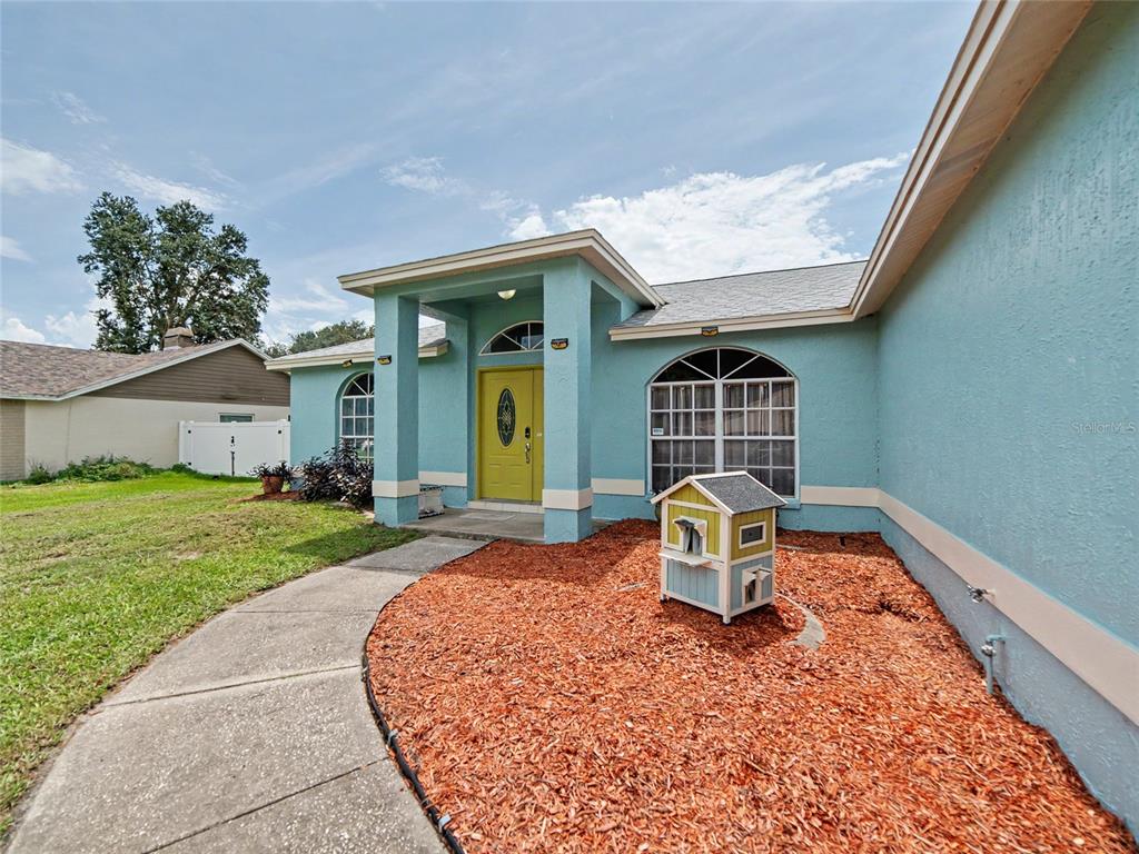 A teal house with a yellow front door and a small wooden playhouse on mulch — 23513 BELLAIRE LOOP, LAND O LAKES, FL