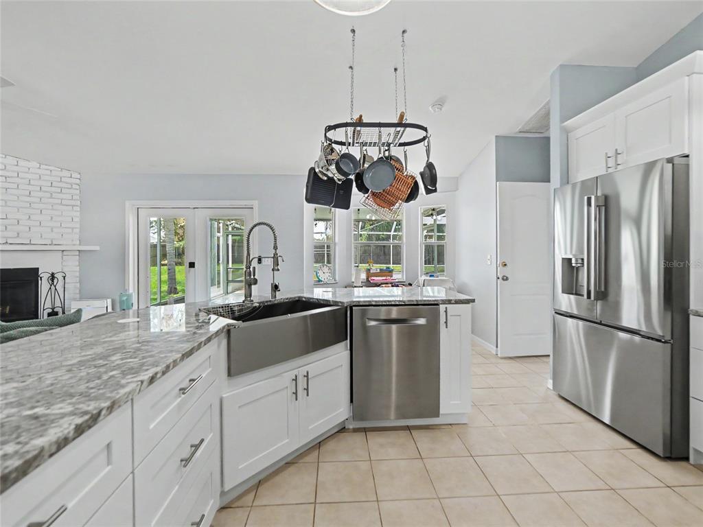 A kitchen features white cabinets, granite countertops, a farmhouse sink, and a hanging pot rack — 23513 BELLAIRE LOOP, LAND O LAKES, FL