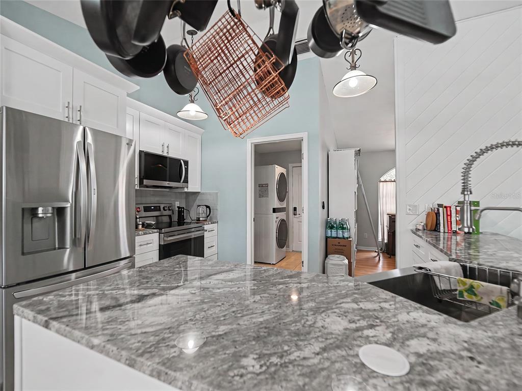 A kitchen features a granite island, stainless steel appliances, white cabinetry, and a hanging pot rack — 23513 BELLAIRE LOOP, LAND O LAKES, FL