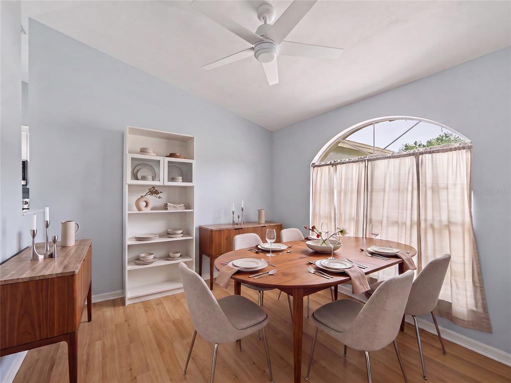 A dining room features a wooden table, light-colored chairs, a white bookshelf, and an arched window — 23513 BELLAIRE LOOP, LAND O LAKES, FL