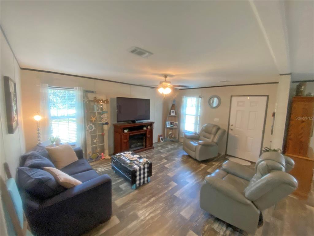 A living room features a dark blue sofa, two grey recliners, and wood-look flooring — 203 SW 5TH AVENUE, PALATKA, FL