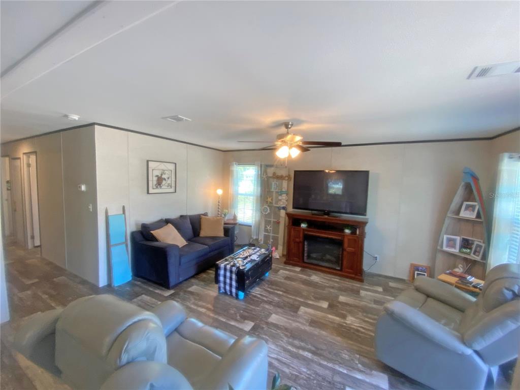 A living room features wood-look flooring, a blue sofa, gray recliners, and a television console — 203 SW 5TH AVENUE, PALATKA, FL